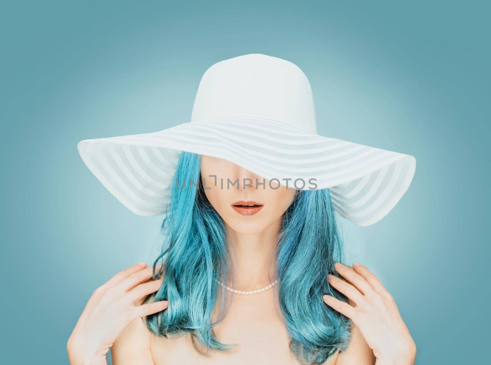 Portrait of young woman with blue hair wearing pearl necklace and in a hat with wide brim, fashion and beauty.
