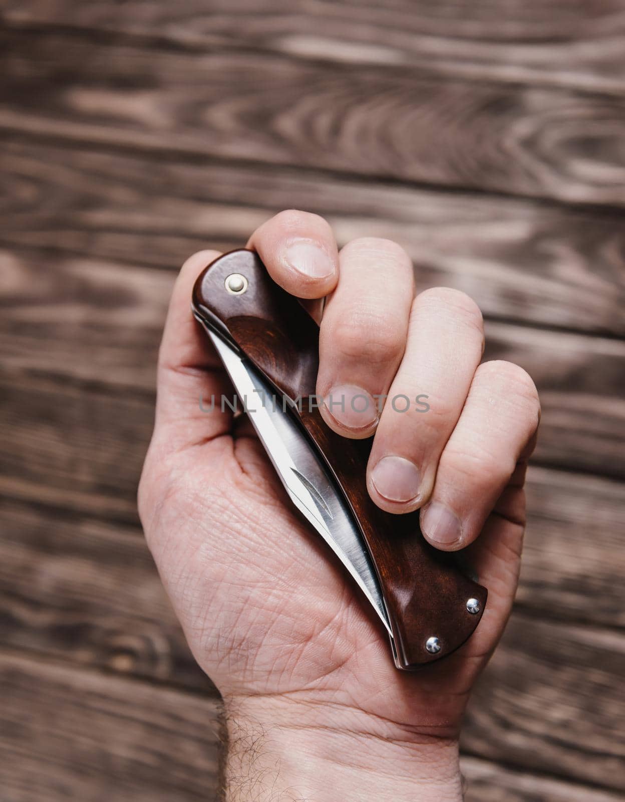 Male hand holding stainless jackknife on a wooden background.