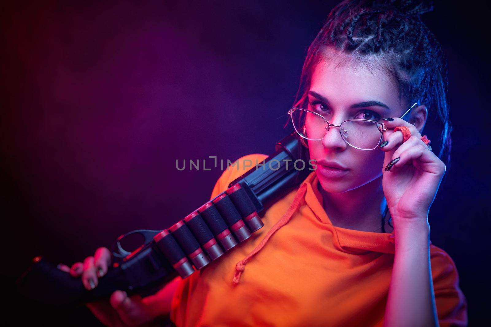 a sexy brunette in an orange jumpsuit with a shotgun on a dark background in neon light