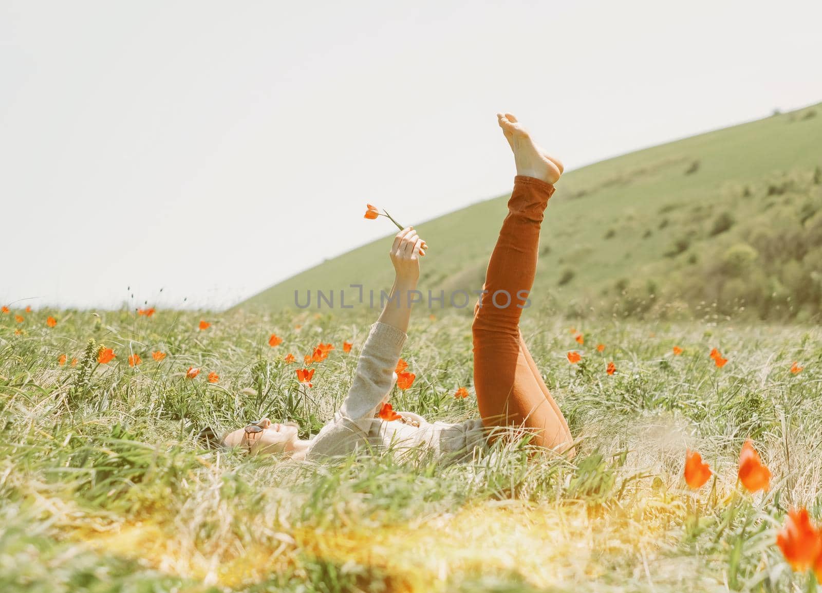 Young woman relaxing on red tulips meadow on sunny day.