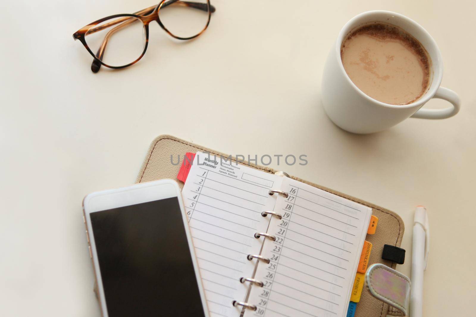 Day planner noter with Mobile phone and notes paper. cozy working place at home. stylish interior in warm pastel colors, table and white coffee mug with glasses. stay at home - a place for home office