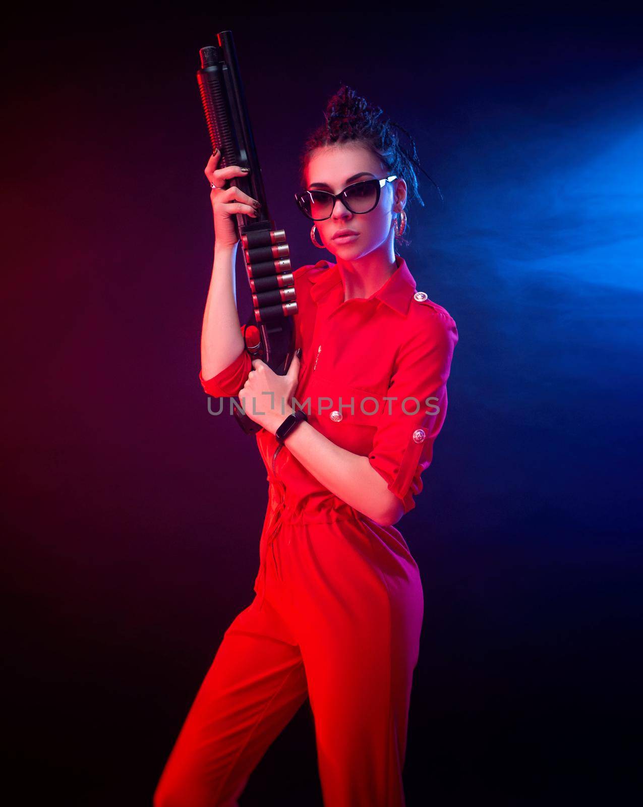 a bright brunette in a red jumpsuit with a shotgun on a dark background in neon light by Rotozey