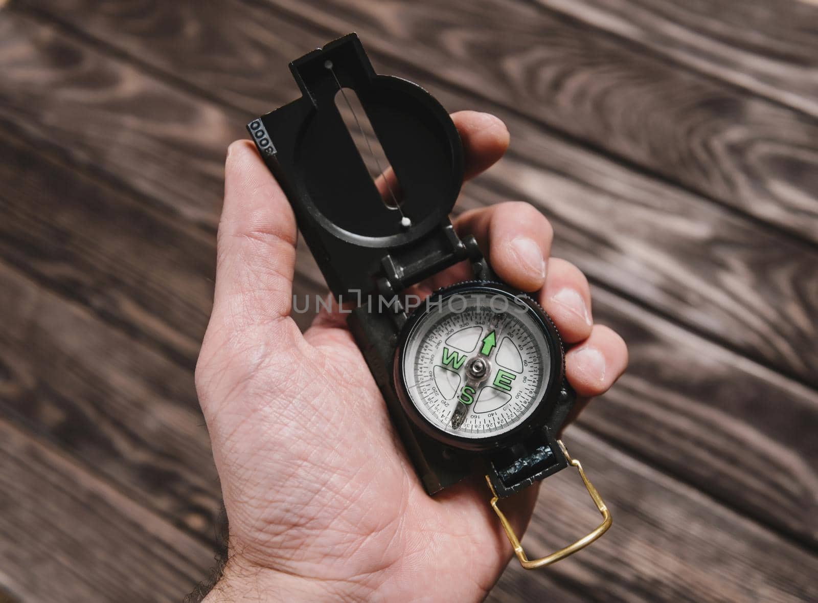 Male hand holding travel compass on a wooden background.