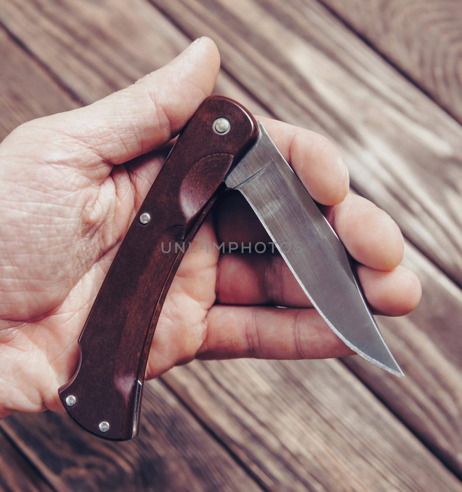 Unrecognizable man holding stainless jackknife on a wooden background, view of hand.
