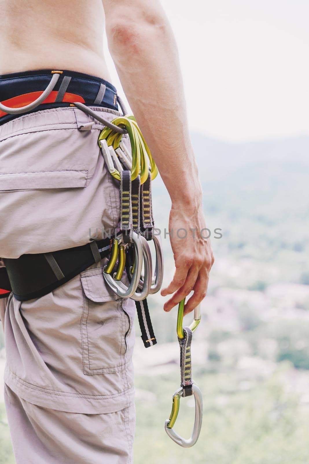 Unrecognizable man climber wearing in safety harness with quickdraws standing in summer outdoor.