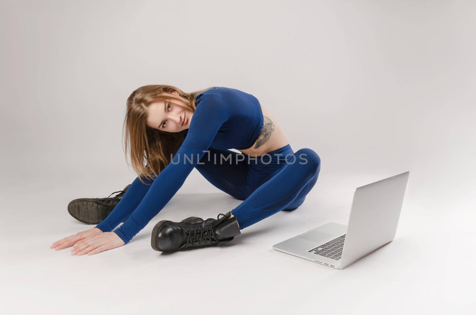 athletic girl posing in the Studio performing exercises online on a laptop on a white background by Rotozey