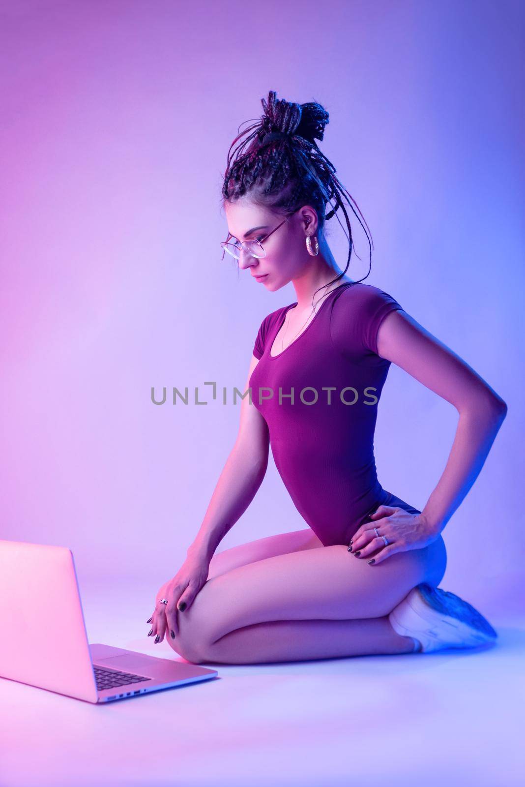 a girl dressed in a bodysuit with dreadlocks on her head is sitting on the floor on a white background in neon light by Rotozey