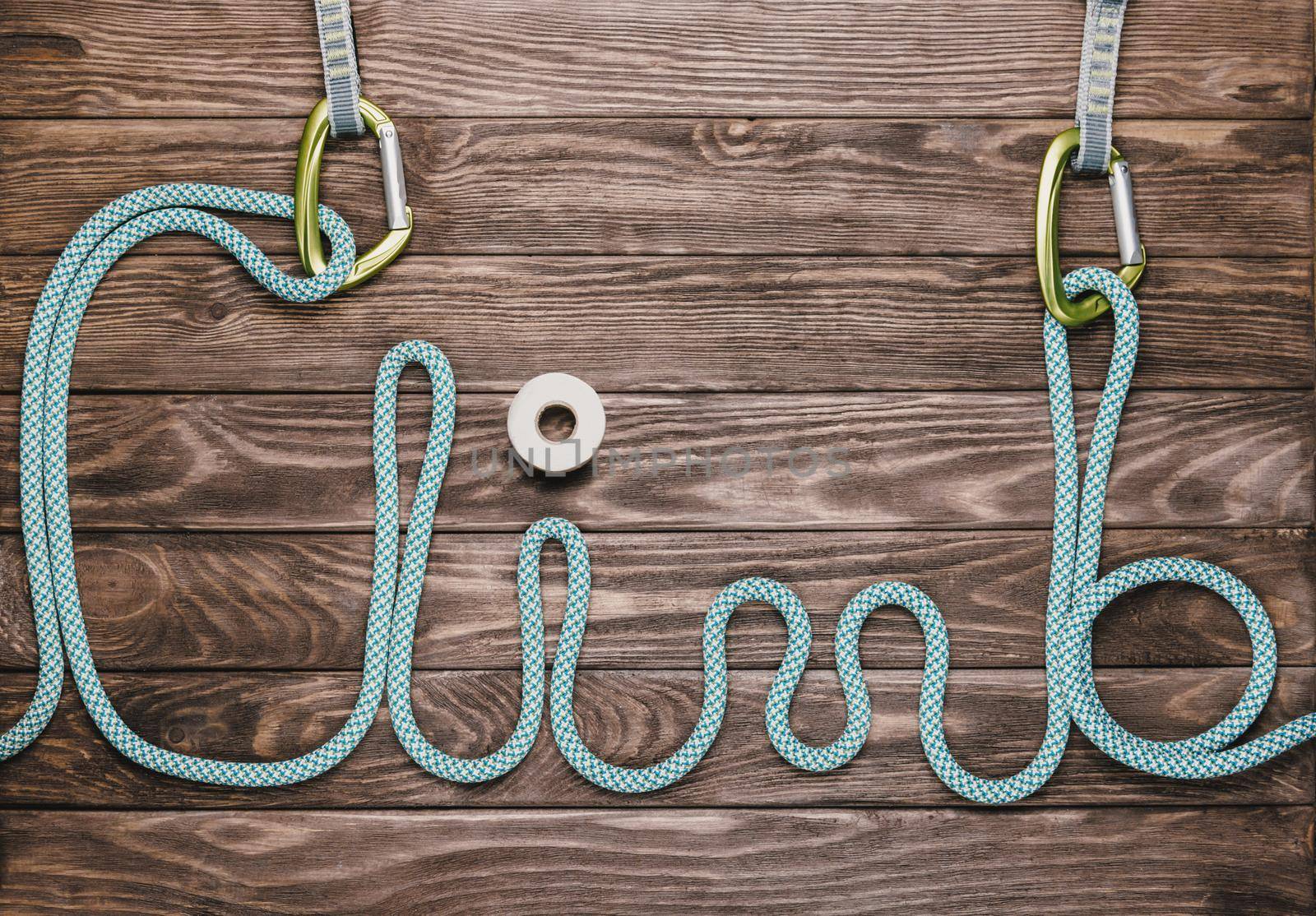Rope in shape of word climb with carbines on wooden background, top view.