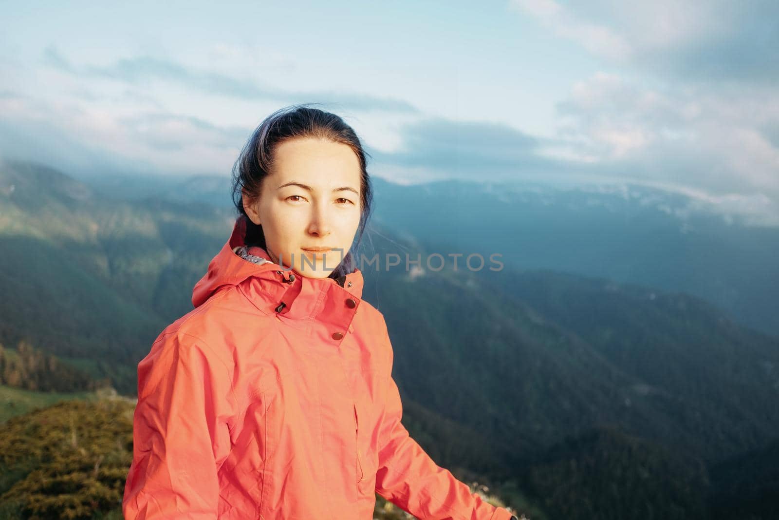 Explorer young woman standing on background of mountains in summer, looking at camera.