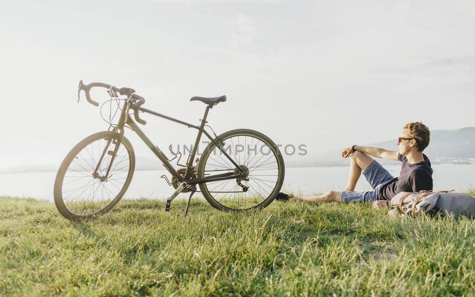 Young man cyclist rests on summer meadow near the bicycle.
