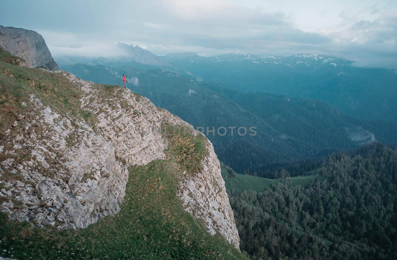 Traveler standing on rocky mountain in summer outdoor. Minimal person in massive landscape.