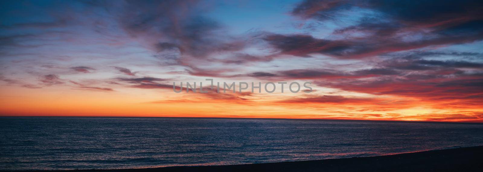 Beautiful sunset over sea in red and yellow colors, cloudy sky.