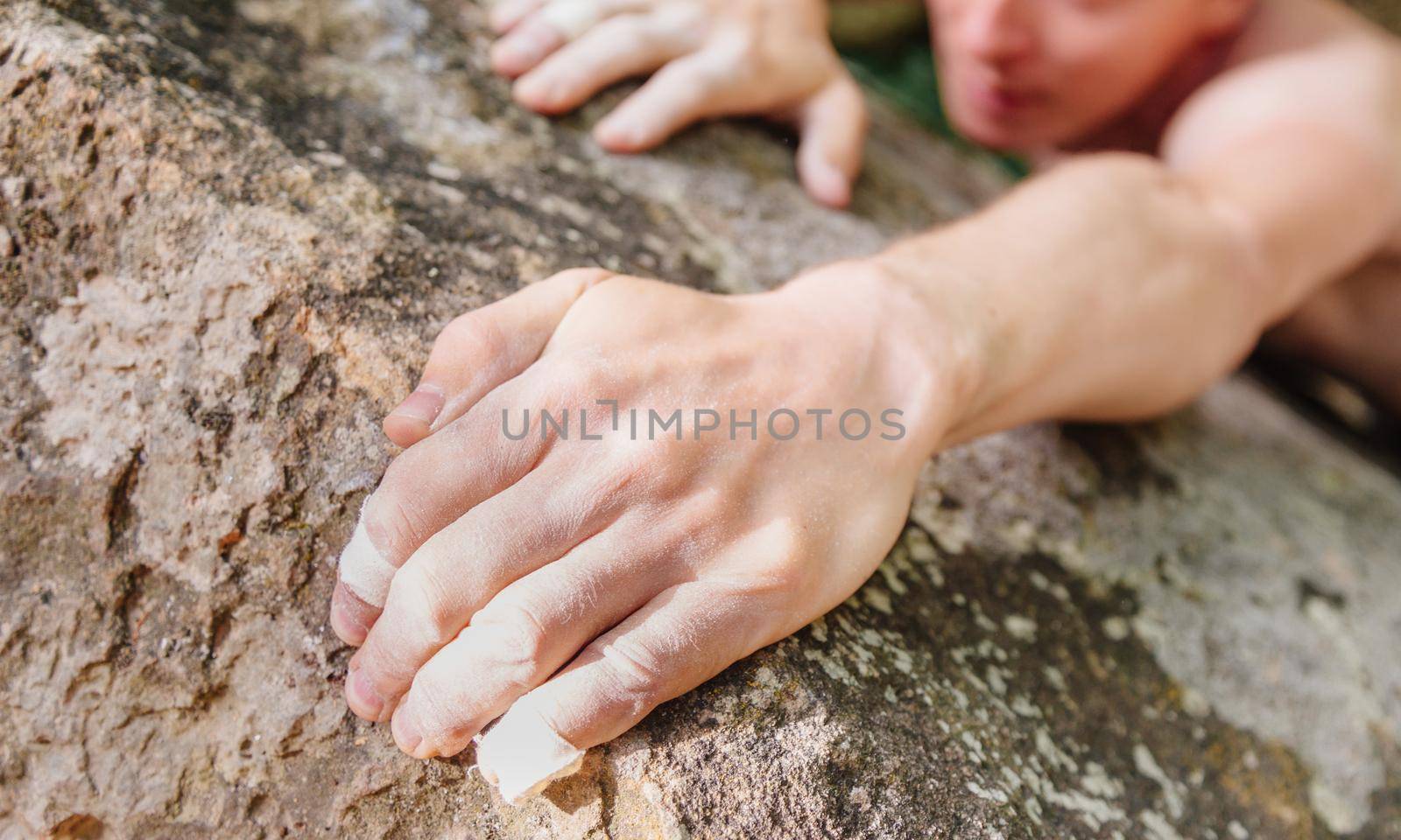 Young man climbing on rock wall, close-up of male hands with tape in magnesium powder.