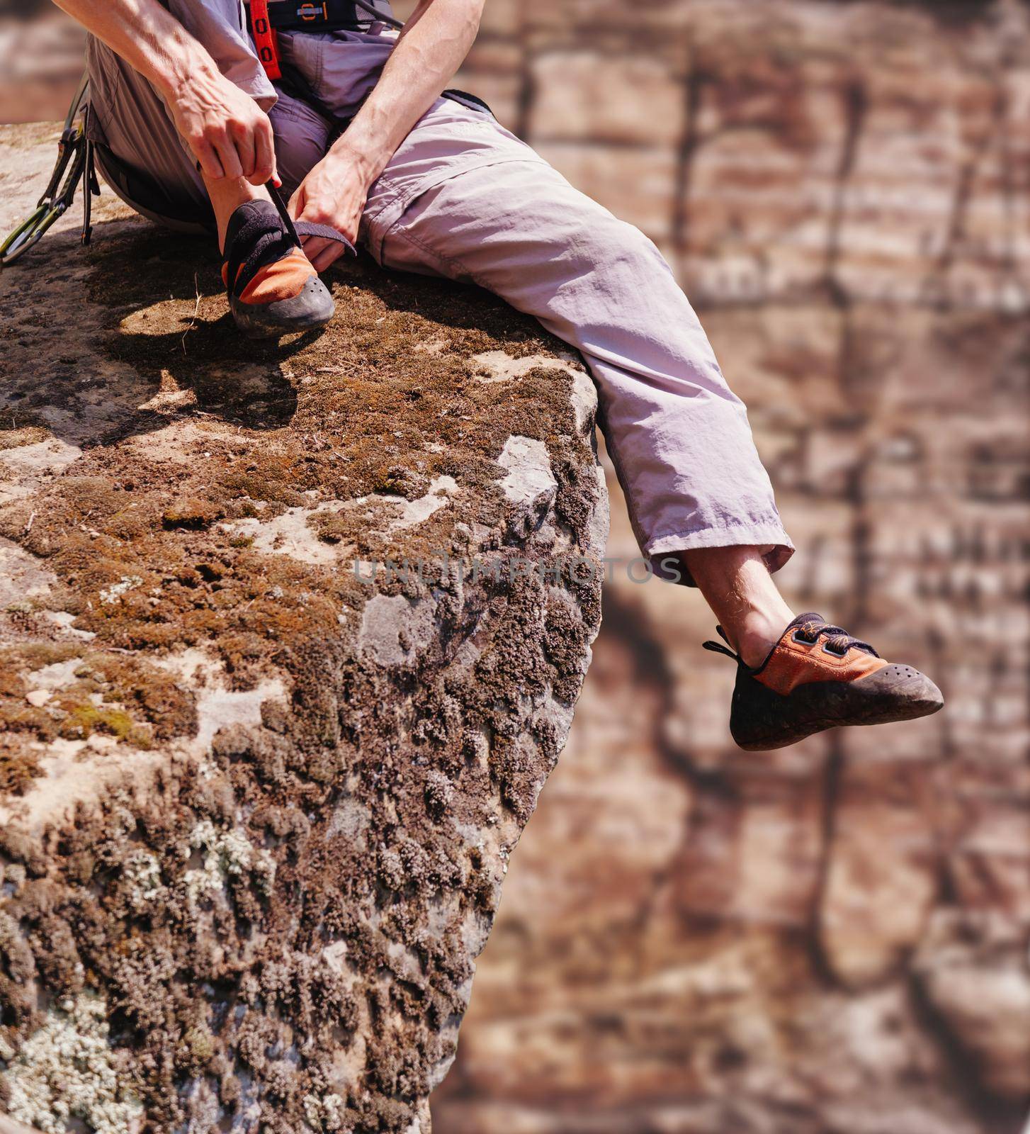 Unrecognizable young man sitting on edge of cliff and putting on climbing shoes.