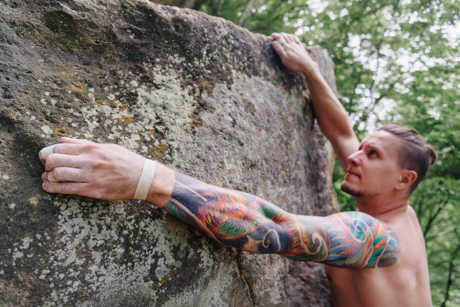 Young man with tattoo on his arm climbing on rock boulder in summer outdoor.