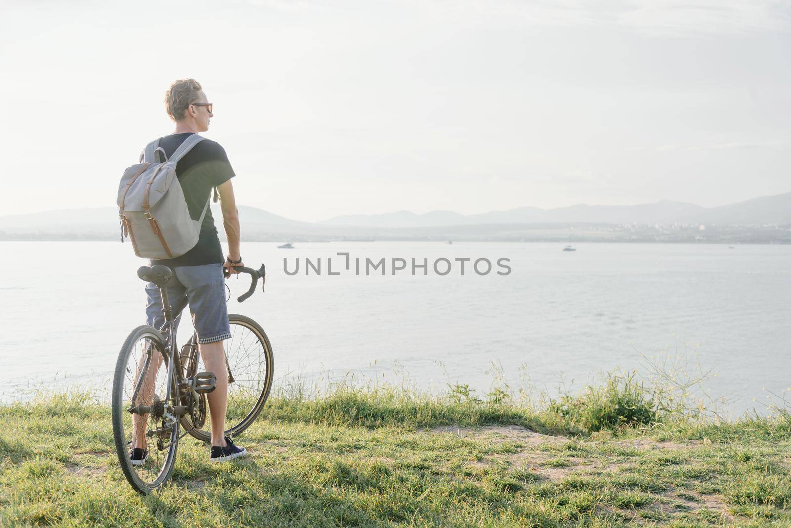 Young man with bicycle standing on coast and enjoying view of sea.