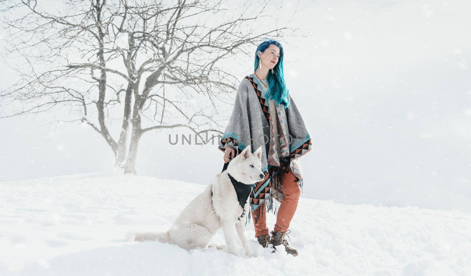Beautiful boho style young woman with blue hair standing with Husky dog in winter outdoor.