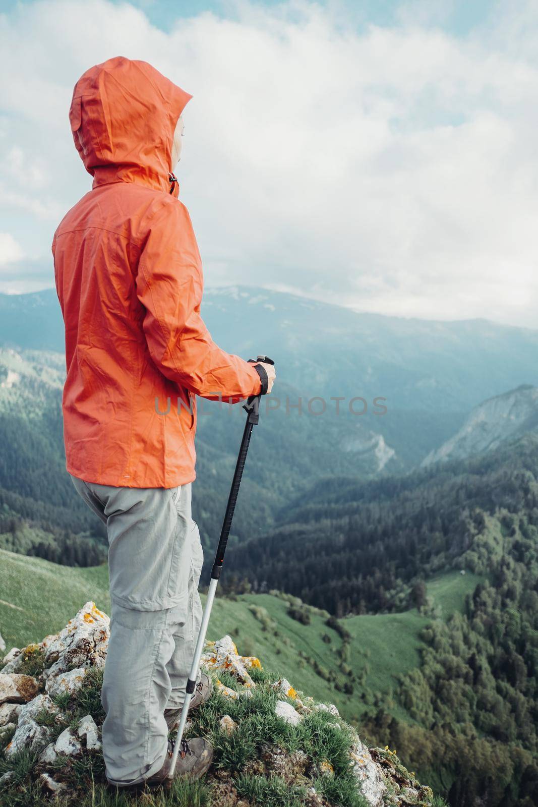 Traveler young woman with trekking poles looking at mountains in summer.