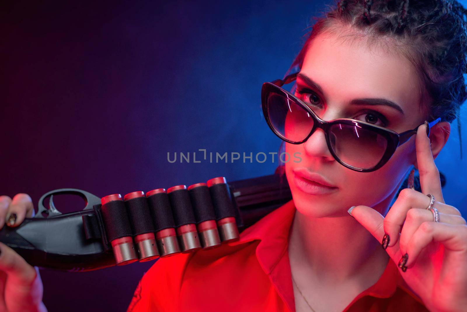 a bright brunette in a red jumpsuit with a shotgun on a dark background in neon light by Rotozey