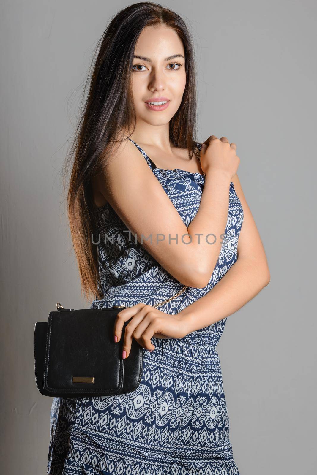 Cute brunette girl with long flowing hair holding a black handbag wearing a sundress with ornament