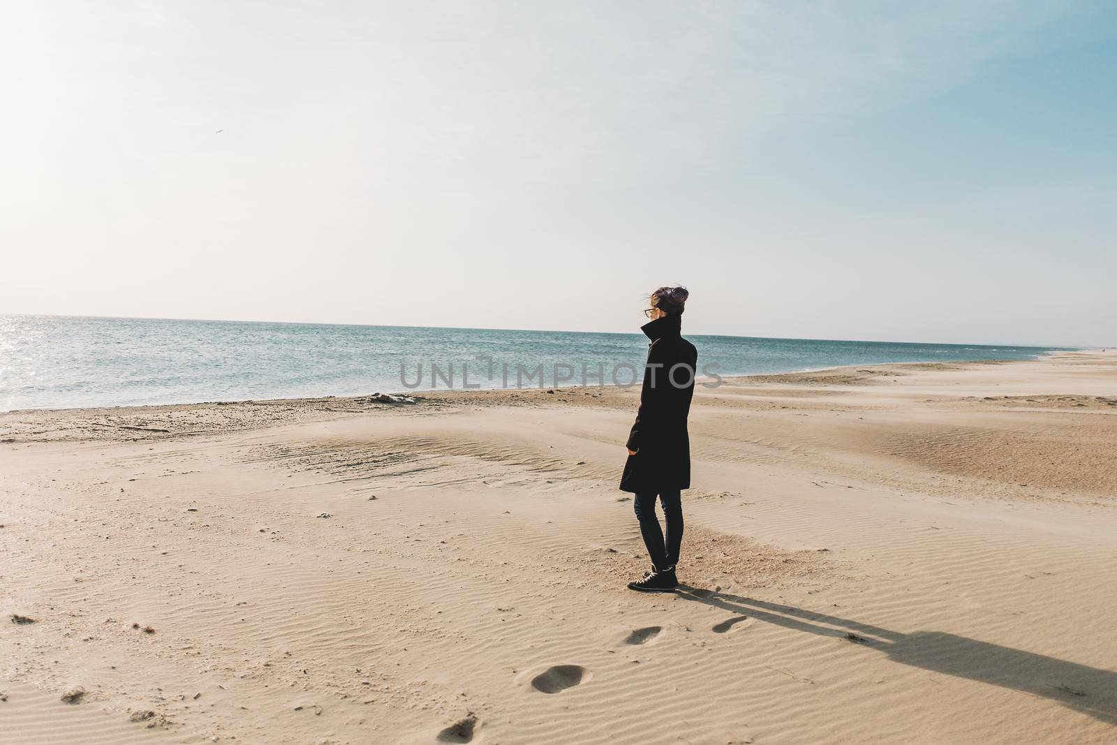 Young woman walking on sandy shore and enjoying view of sea in autumn.