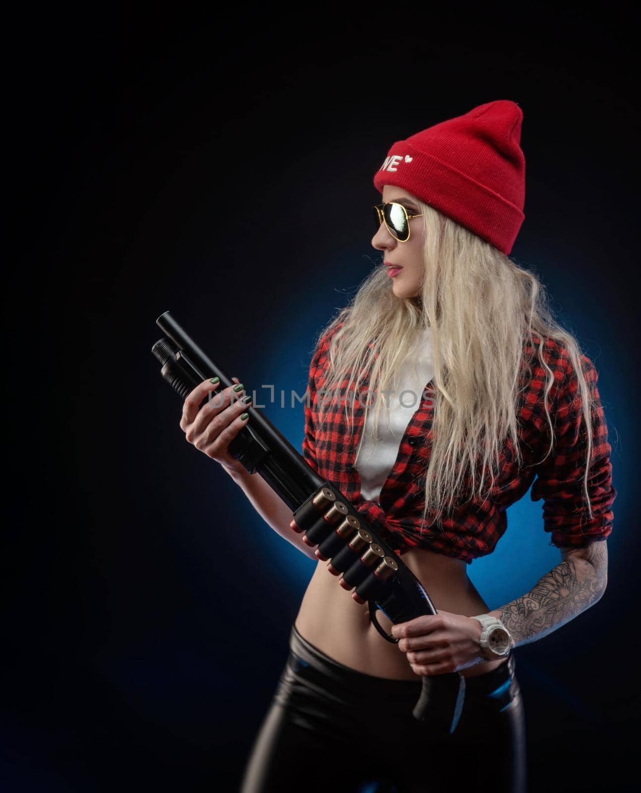 bright blonde in a red hat with a shotgun on a dark background