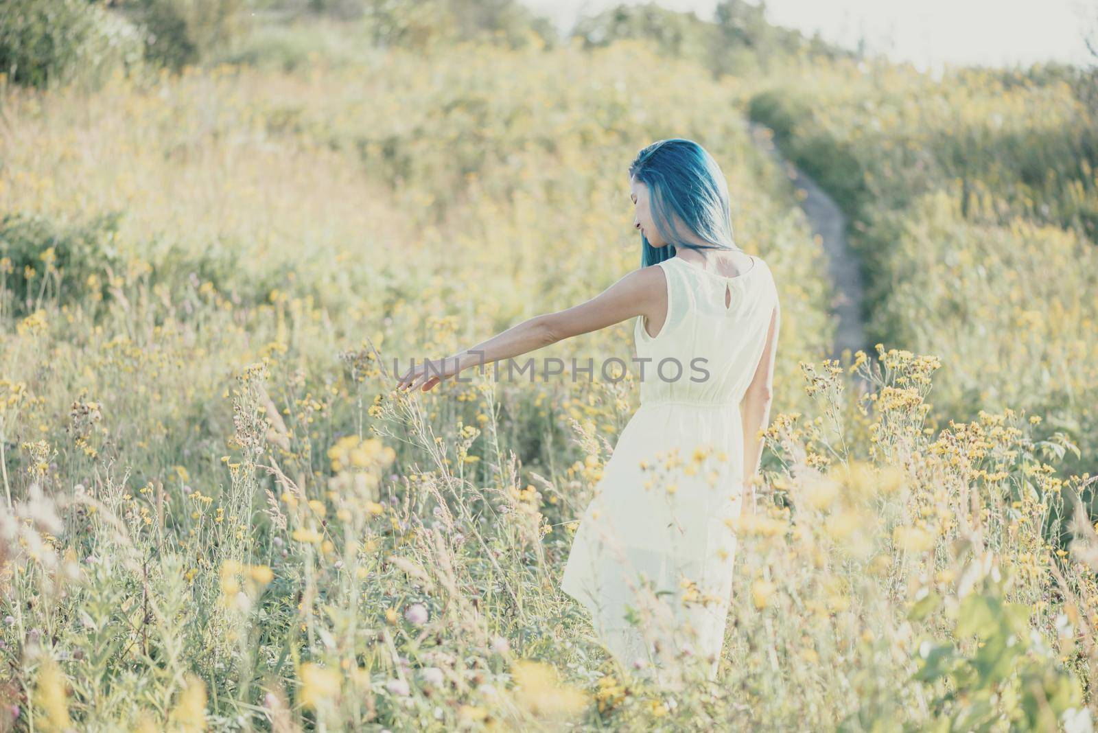 Beautiful young woman walking on yellow wildflower meadow in summer.