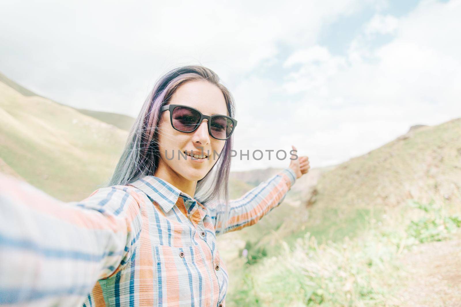 Happy young woman taking self-portrait in summer mountains, point of view.
