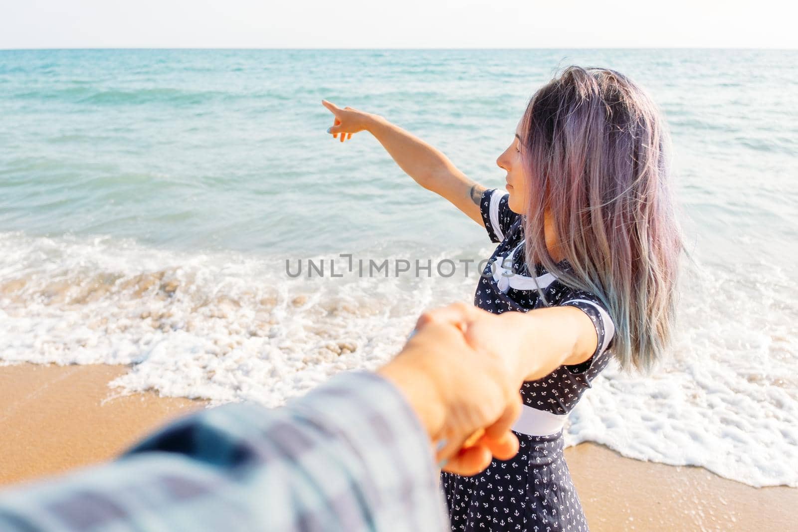 Couple in love. Beautiful young woman holding man's hand and pointing at sea. Point of view shot.