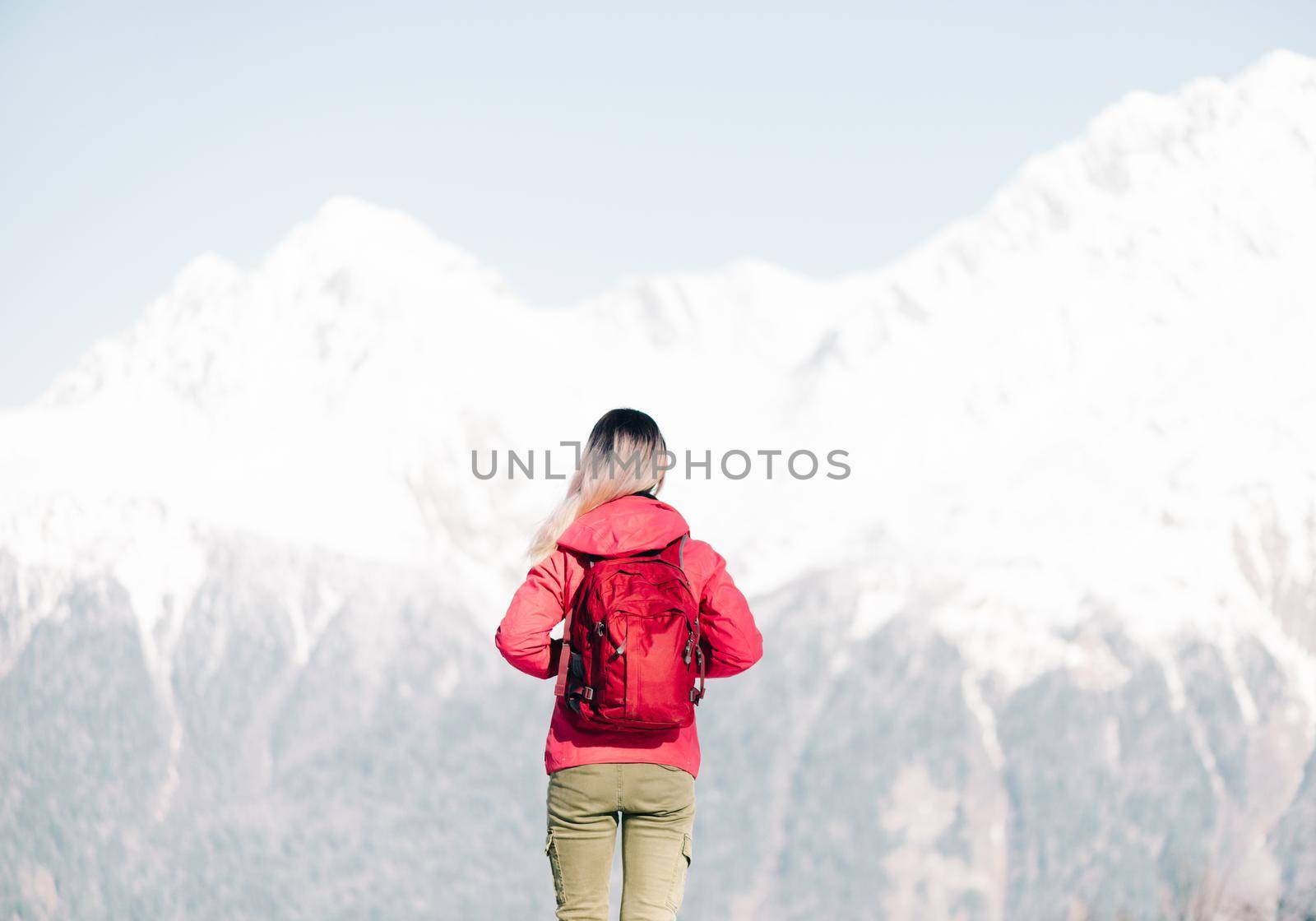Backpacker young woman standing in front of winter mountains, rear view.