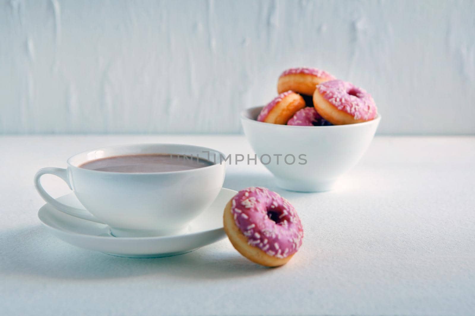 Mug of hot cocoa and donuts on white background. Tasty pink donuts and cacao cup. Sweet breakfast