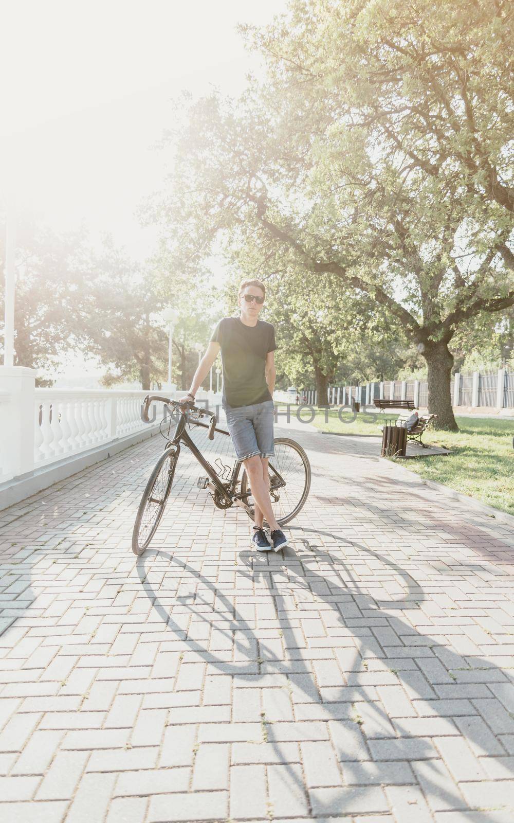 Handsome young man standing with bicycle in summer park.