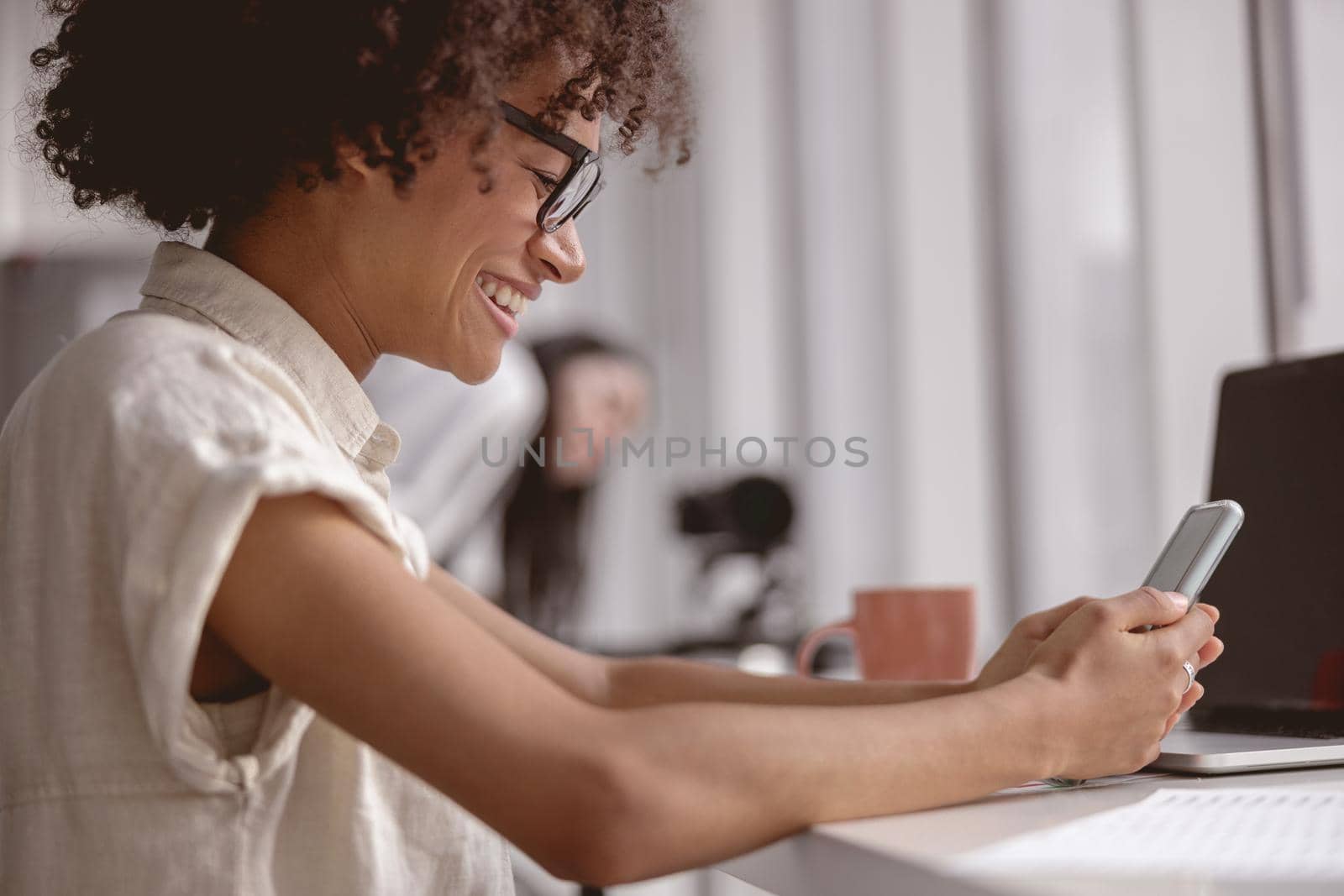 Side view happy female worker typing on smartphone while sitting at workplace