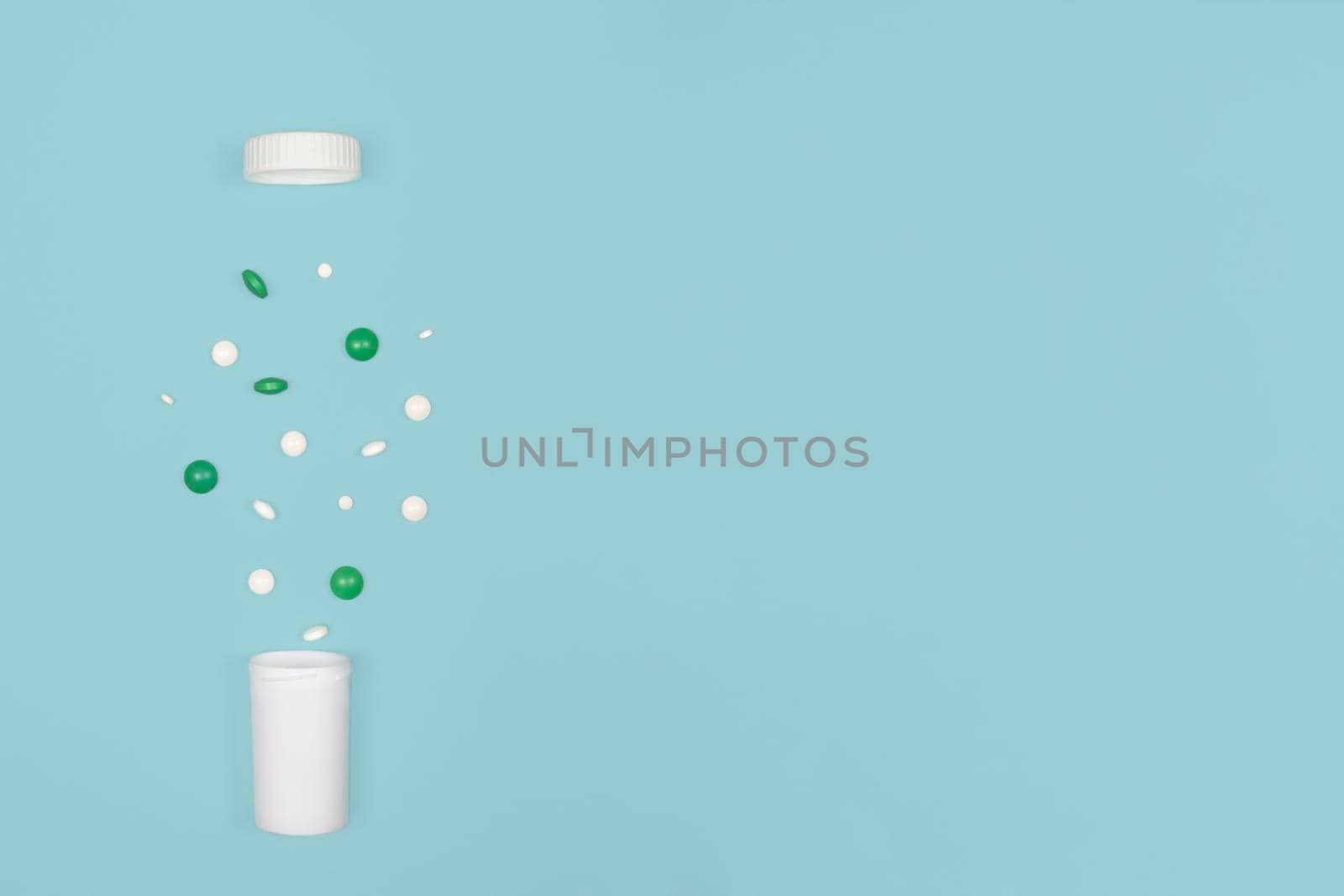 Medical background with pills. White and green pills pour out of a bottle on a blue background. Flat lay concept. Copy space.