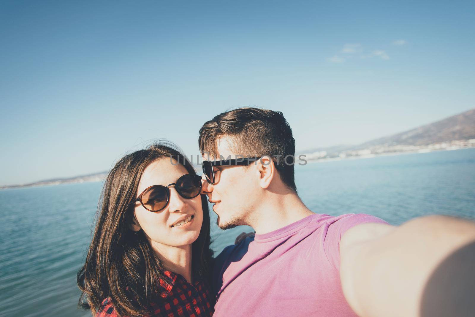 Young loving couple in sunglasses taking selfie on background of sea in summer, point of view.