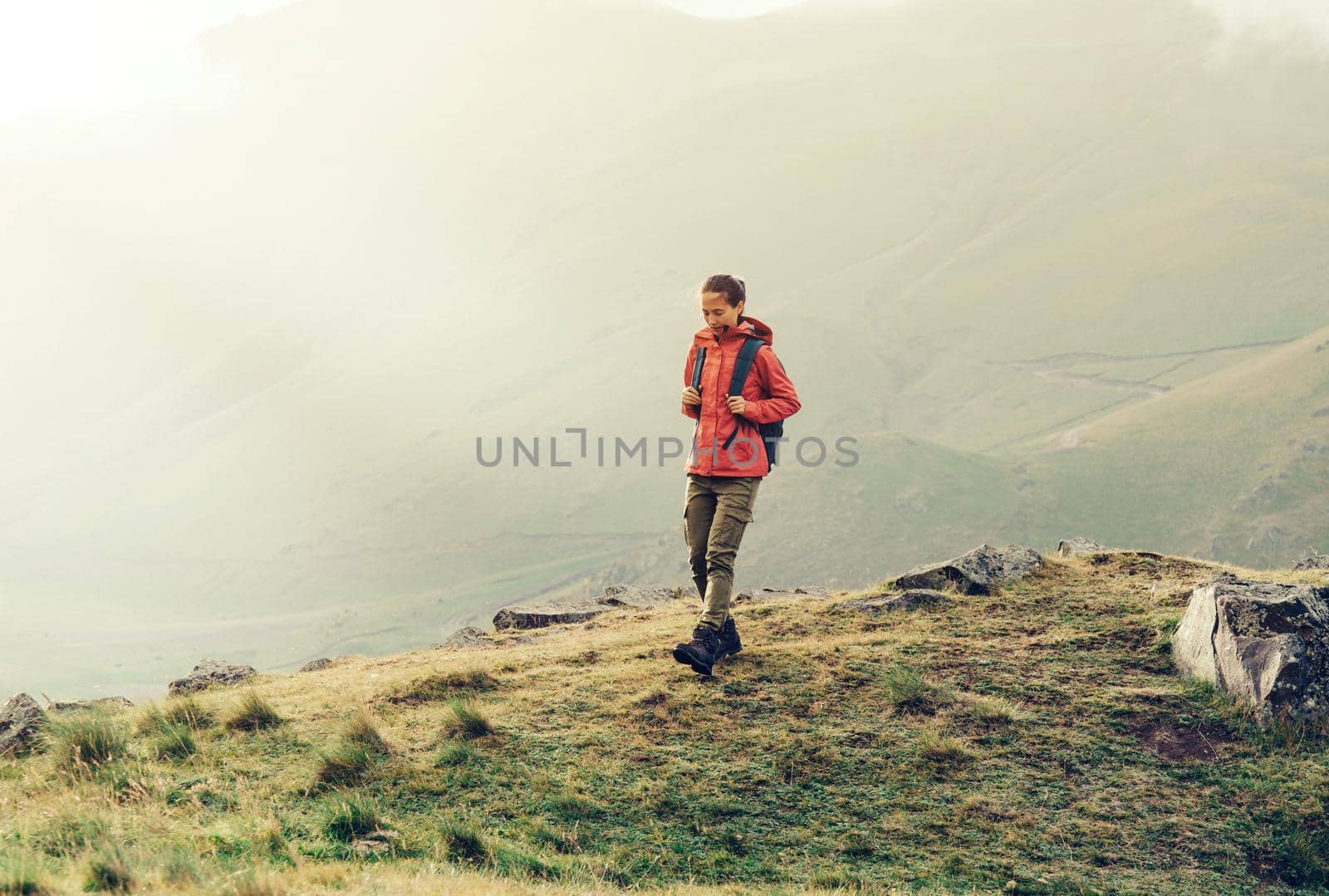 Hiker young woman with backpack walking in the mountains in fog weather.