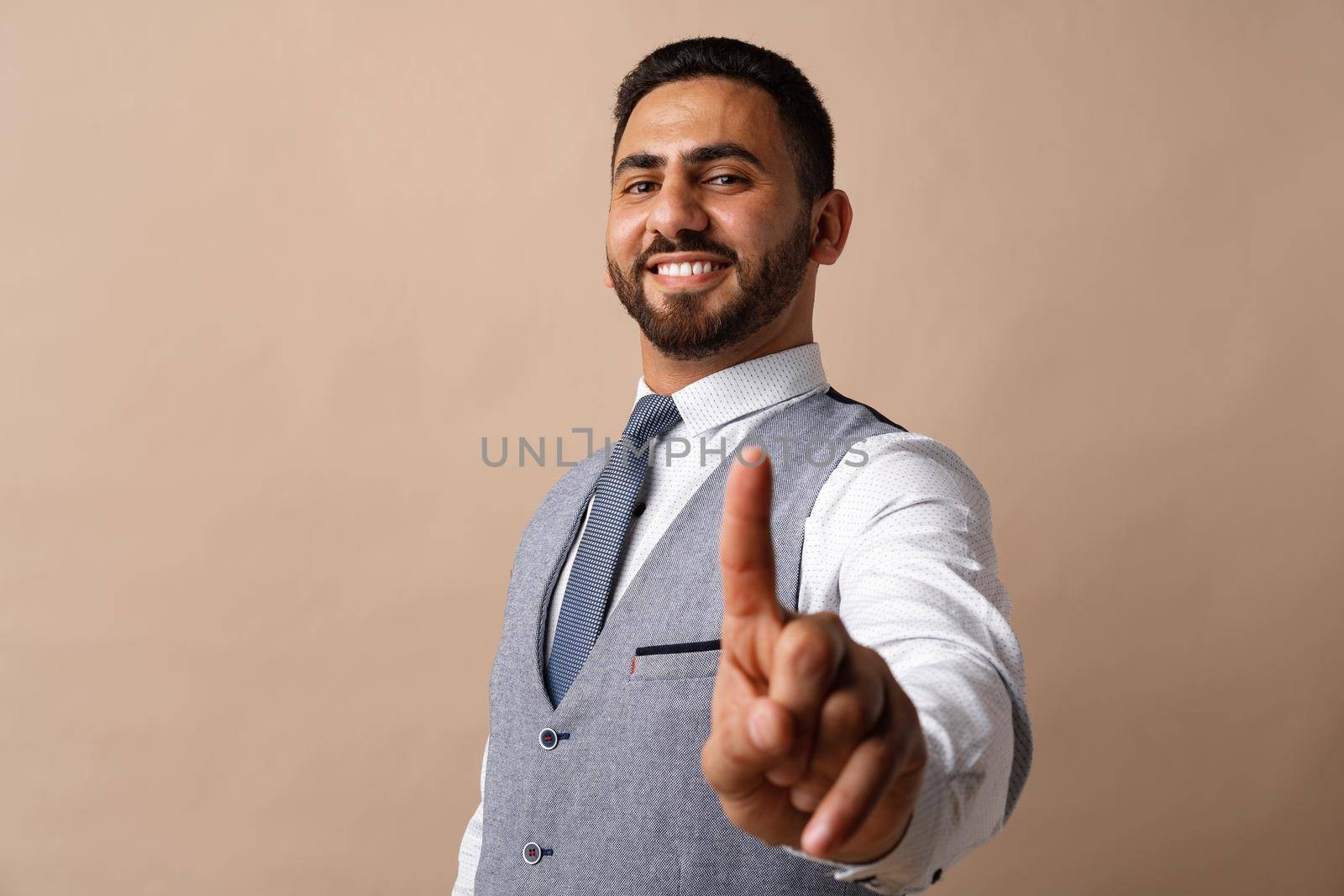 Young arabian businessman pointing finger to camera against beige background, close up