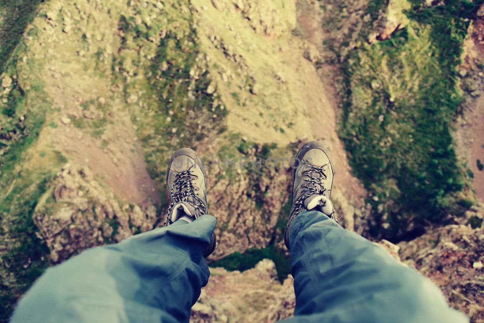 Hiker man sitting on edge of cliff in the mountains, view of legs, pov image.