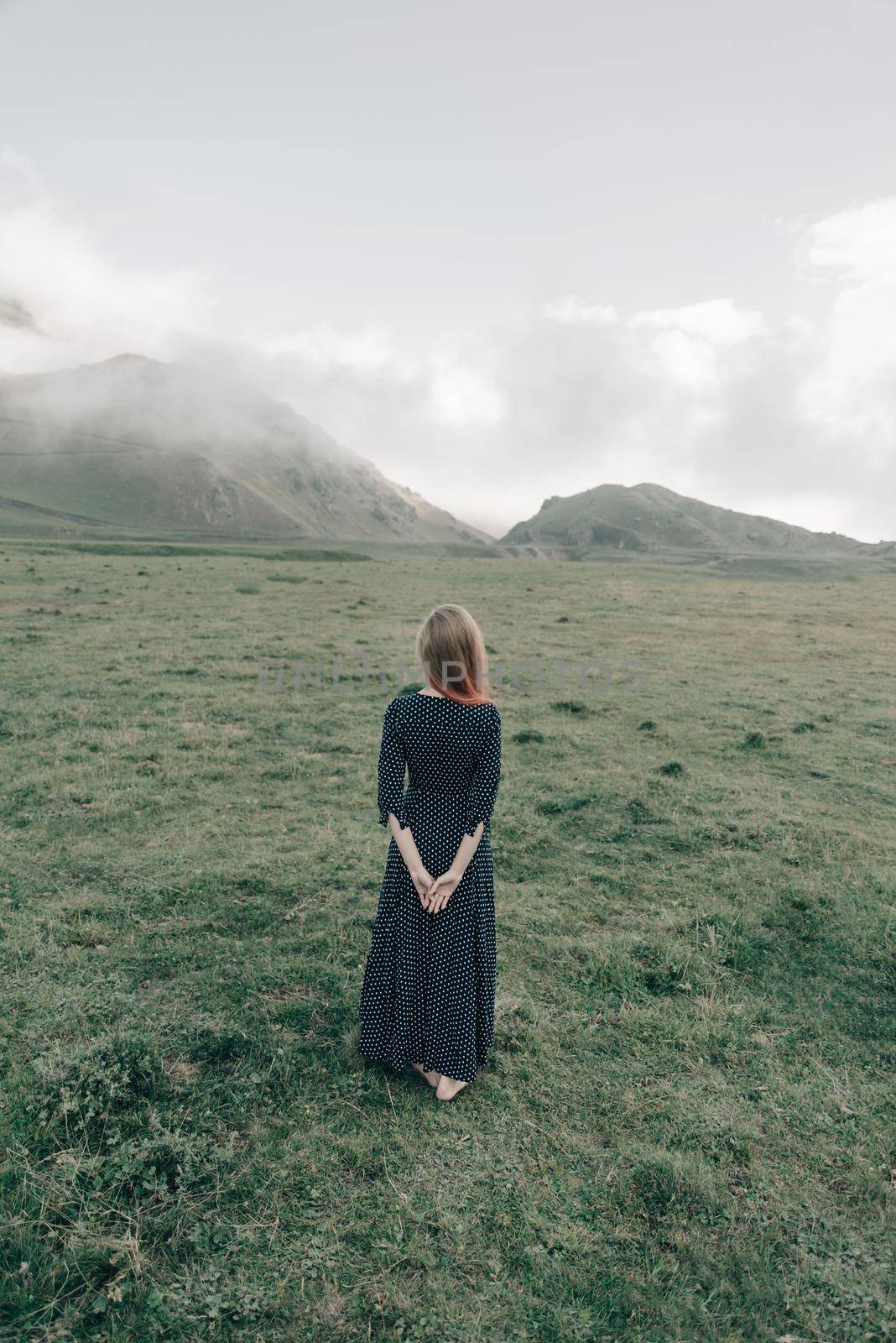 Young woman wearing in long dress walking in summer mountains, rear view.