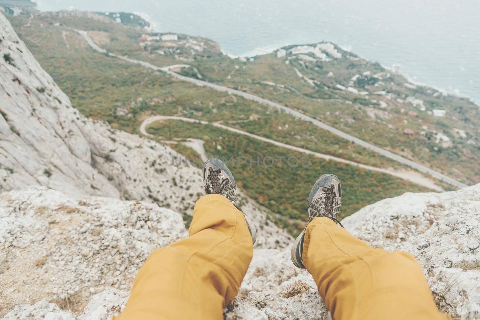 Man sitting on edge of cliff over coastline, view of legs, pov.