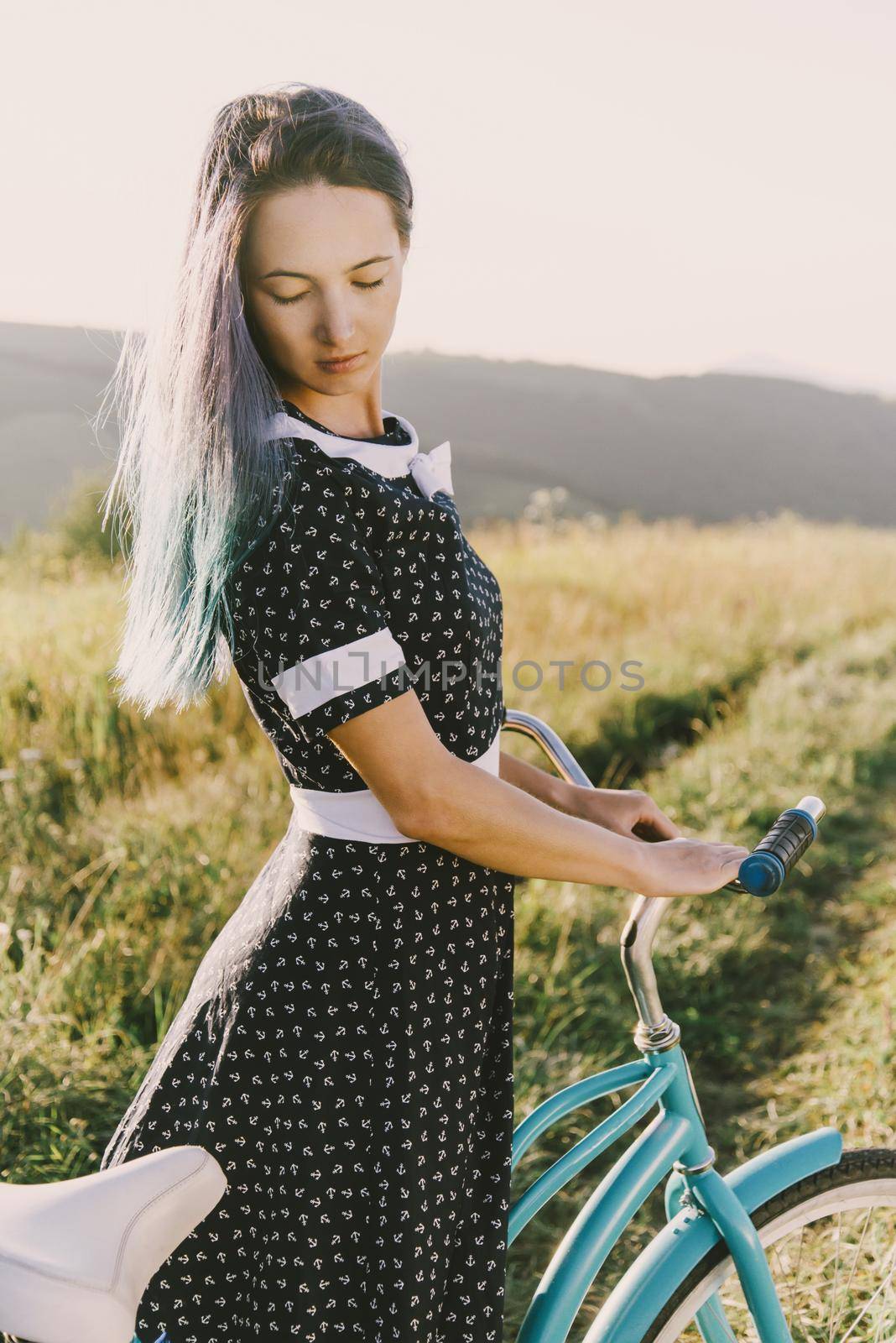 Beautiful young woman in dress standing with bicycle cruiser outdoor.