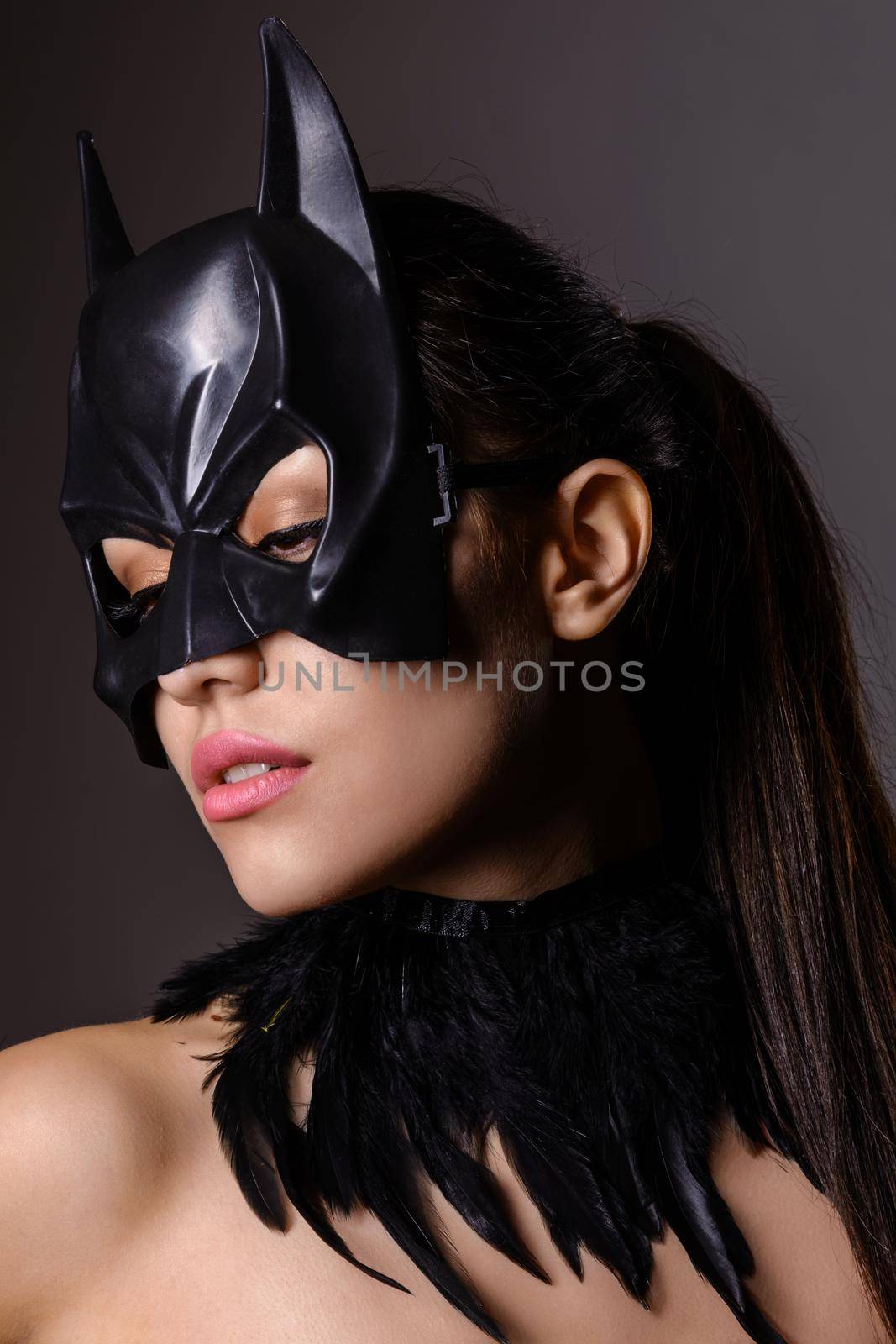 Portrait of charming brunette girl in Batman mask on a gray background