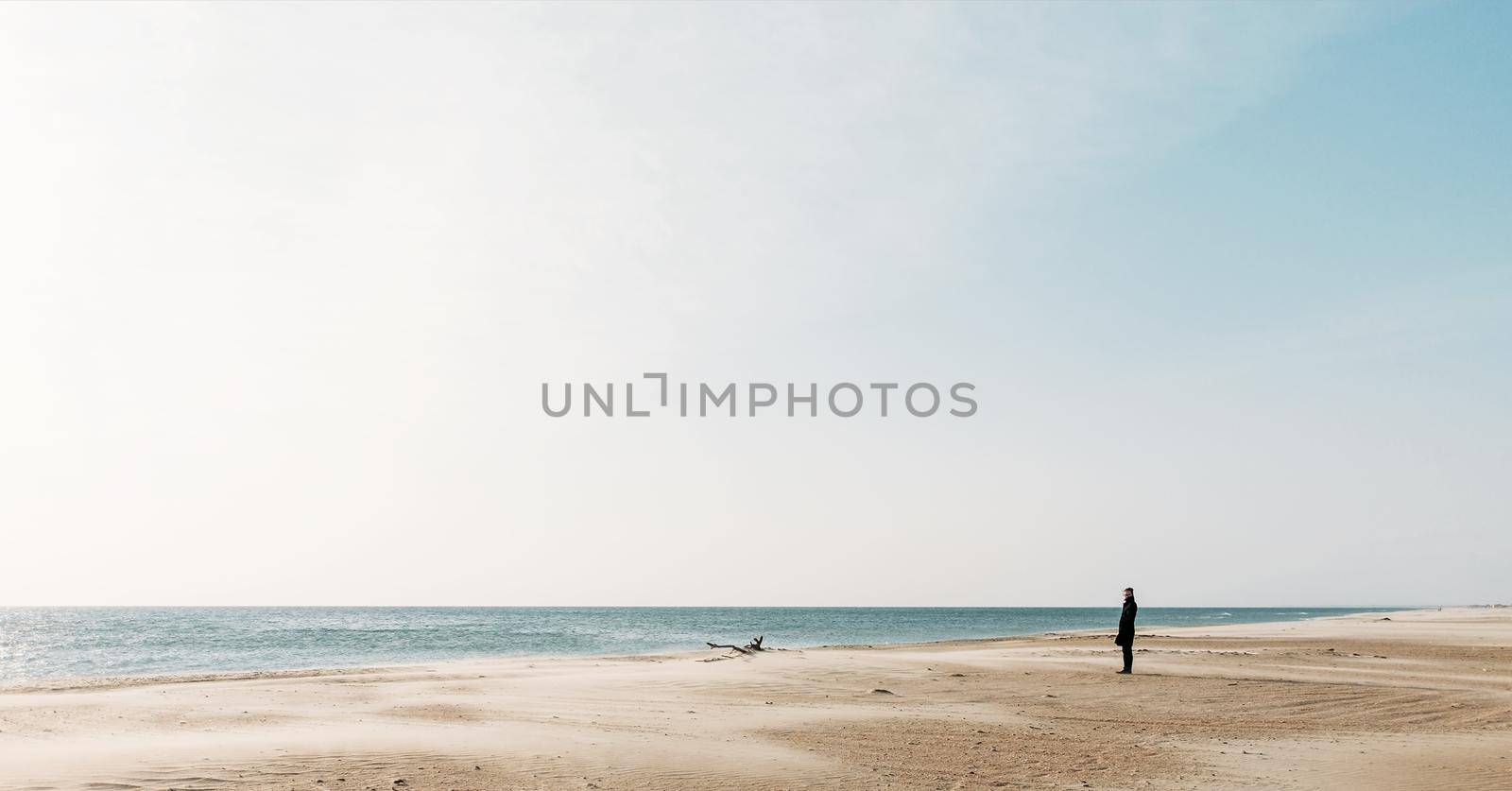 Lonely young woman walking on sandy coastline and enjoying view of sea.