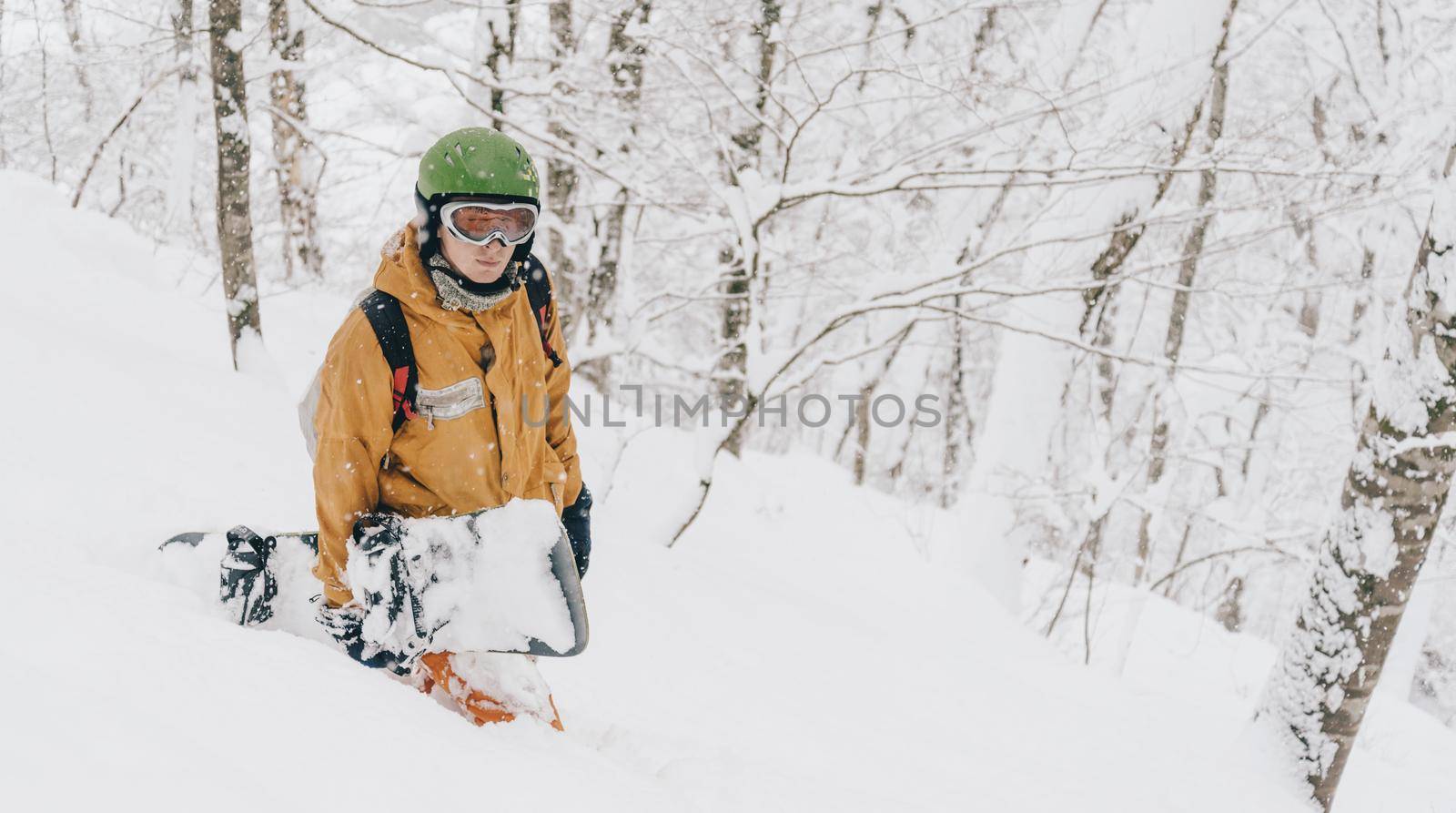 Sporty young man wearing in protective clothing walking with snowboard in winter forest after a snowfall.