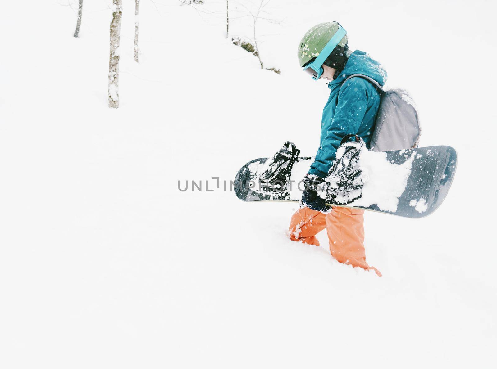 Female freerider wearing in protective clothing walking with snowboard in winter forest after a snowfall.