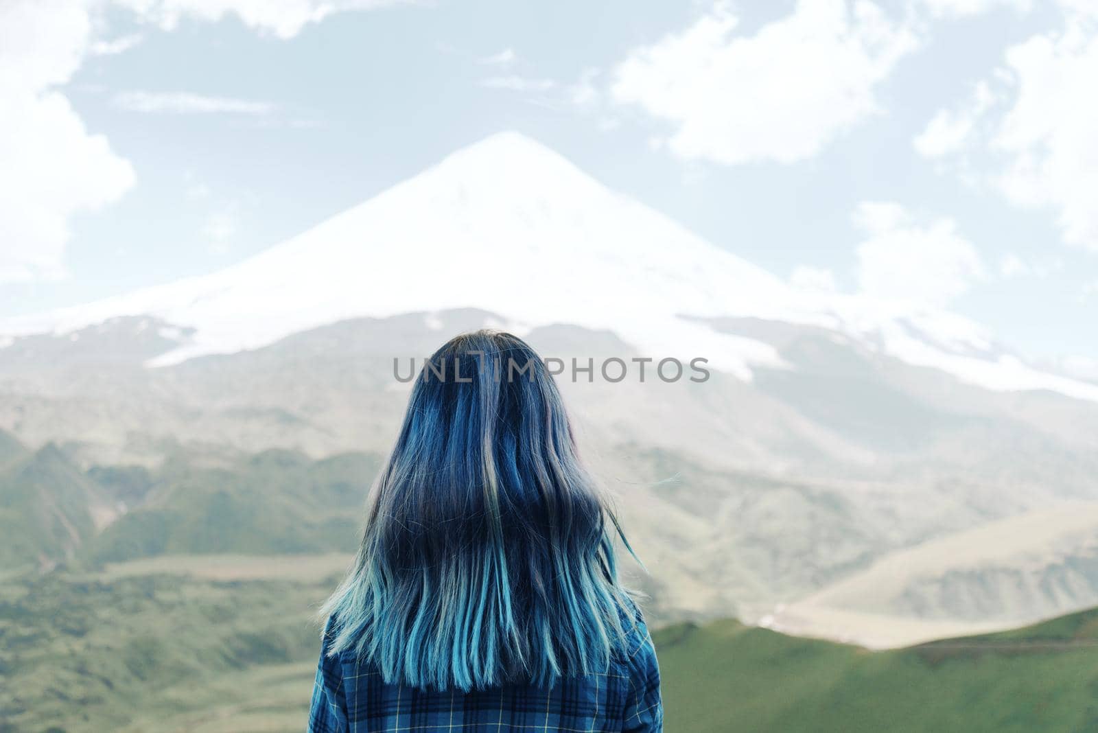 Young woman with blue hair looking at snowy mountain, rear view.