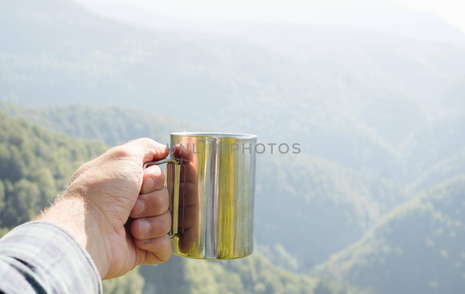 Traveler man drinking tea in the mountains. View of male hand with cup outdoor. Point of view shot.
