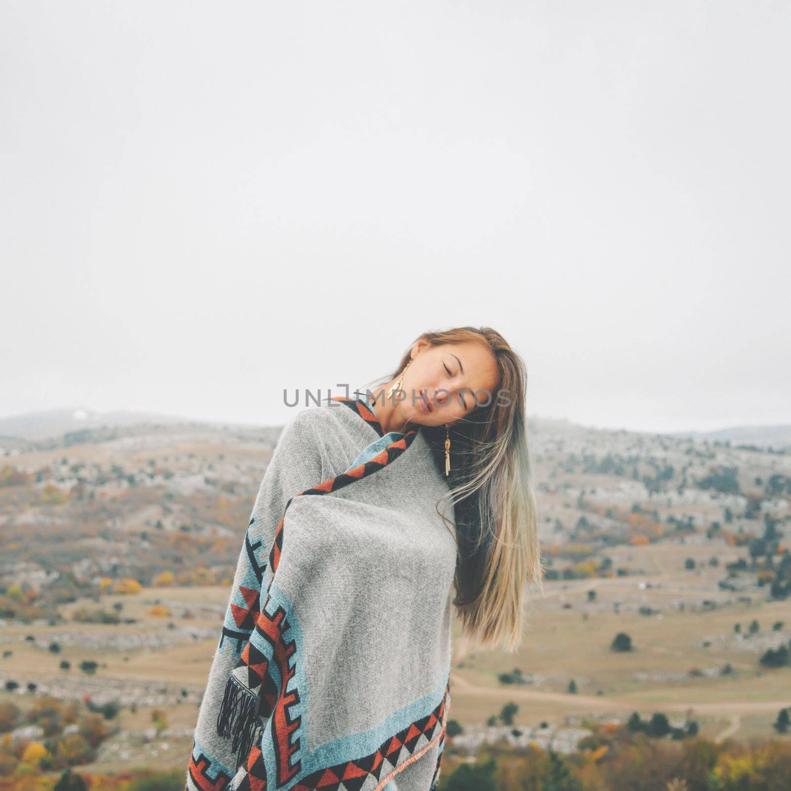 Beautiful young woman wearing in poncho standing with closed eyes on autumn nature.
