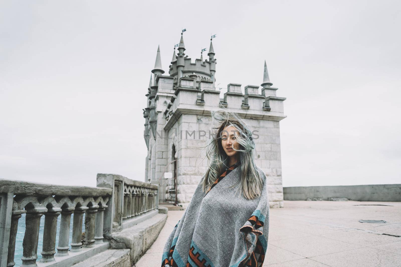 Young woman standing on background of castle Swallow's Nest in windy weather, Crimea, Russia