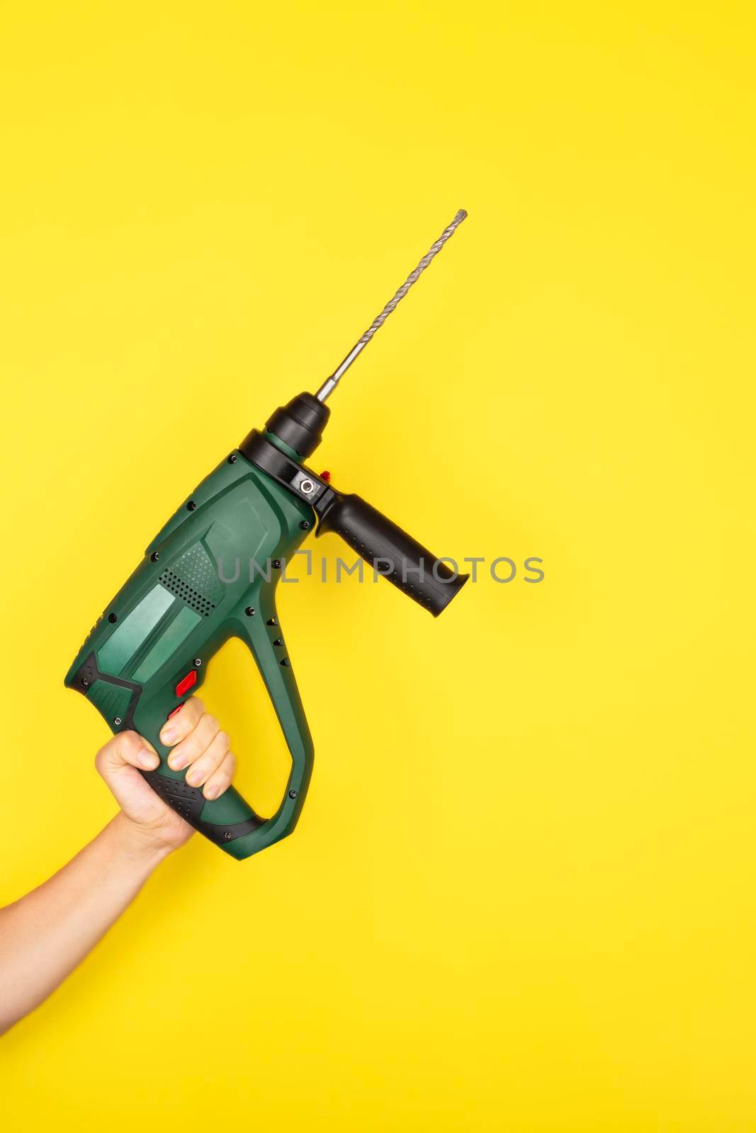 Green Puncher in the hands of a builder. Female hand hold new Puncher or drill isolated on yellow background